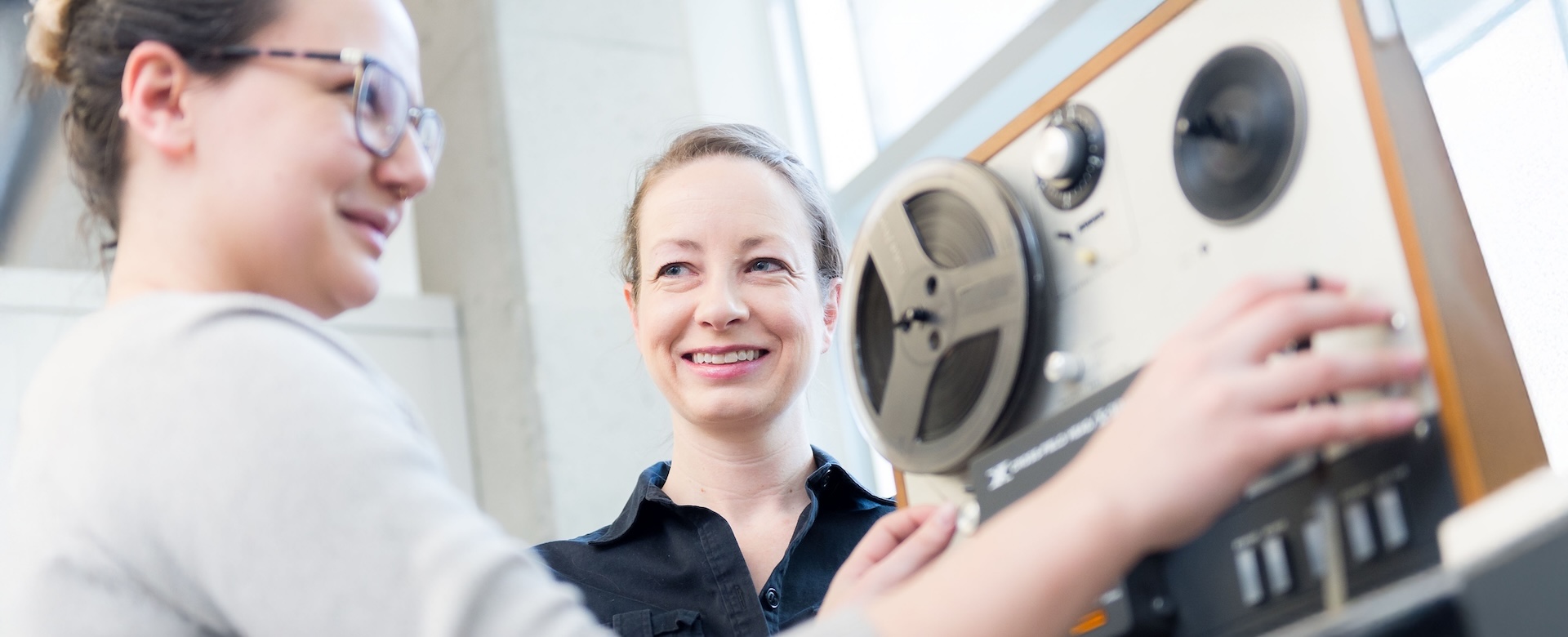 A student operates sound recording equipment with a smiling professor.