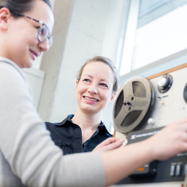 A student operates sound recording equipment with a smiling professor.